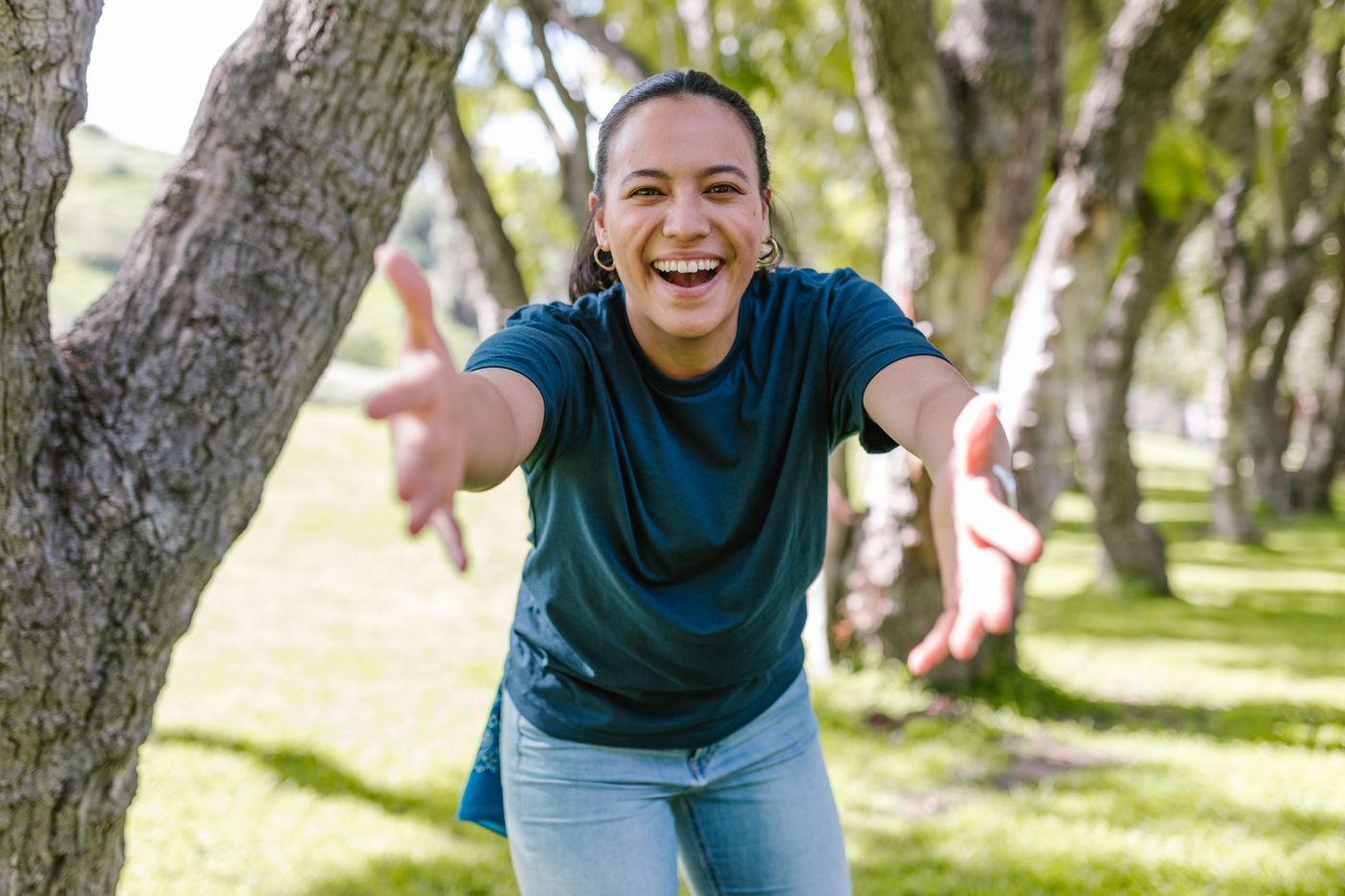A smiling woman reaching out with open arms in a park