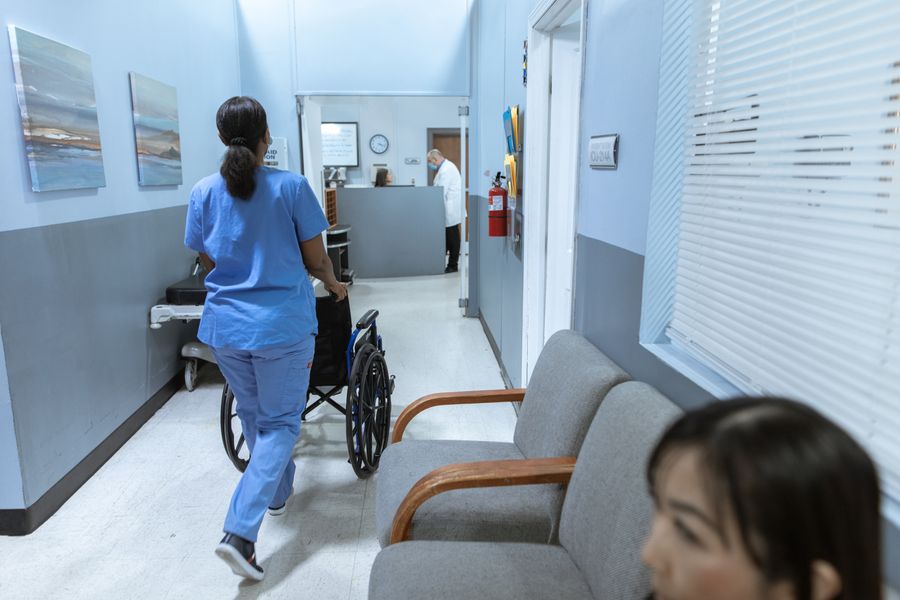 A nurse pushing a wheelchair along a hospital corridor