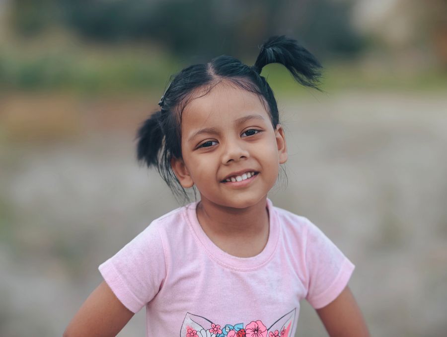 A smiling young girl in a pink shirt outdoors